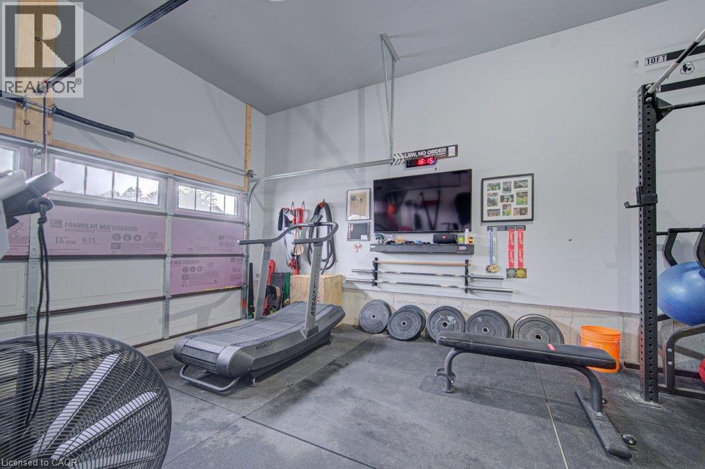 Dedicated fitness space featuring rubber flooring, wall-mounted television, and overhead garage door with upper window panels - 15 Matheson Crescent, Innerkip, ON - Indoor Photo Showing Garage
