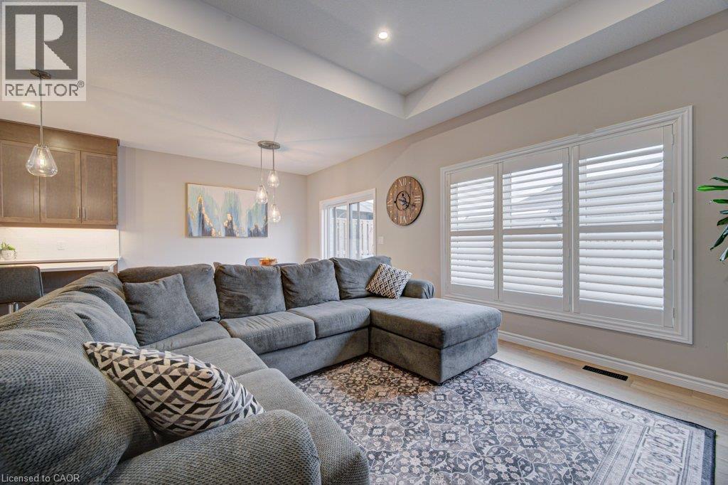 Open-concept living space featuring a tray ceiling with recessed lighting, light wood-finish flooring, and white plantation shutters - 15 Matheson Crescent, Innerkip, ON - Indoor Photo Showing Living Room