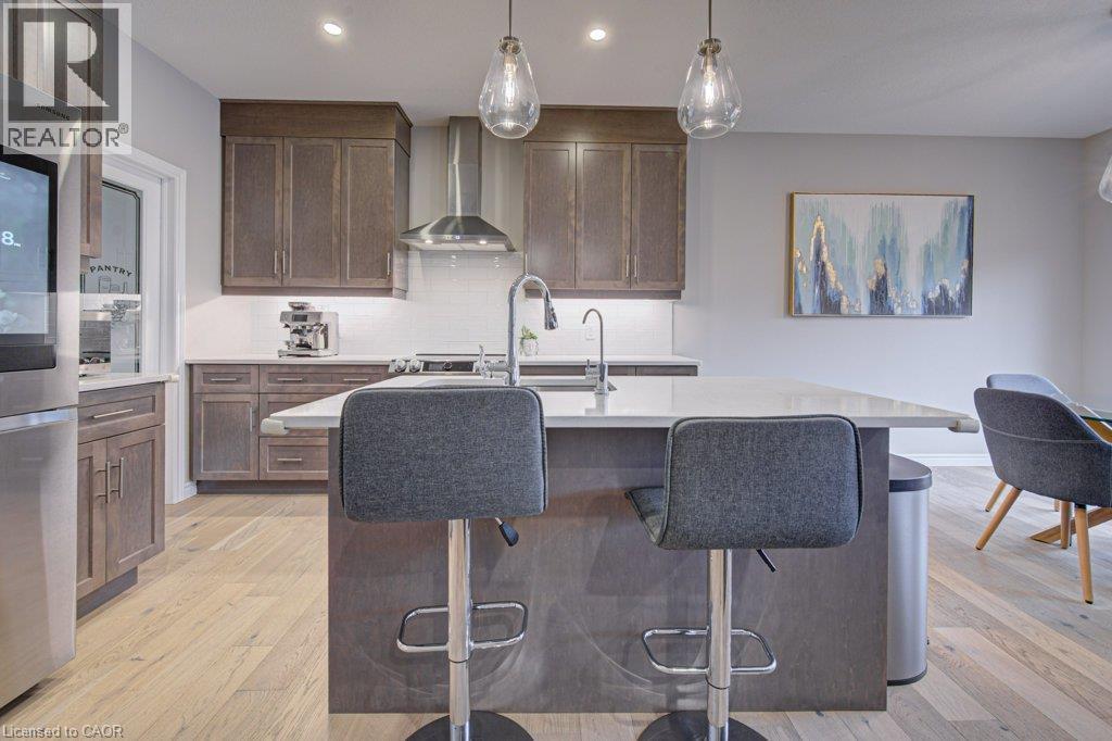 Kitchen featuring an expansive island with a light-toned countertop, wood-finish cabinetry, stainless steel appliances, and wood-finish flooring - 15 Matheson Crescent, Innerkip, ON - Indoor