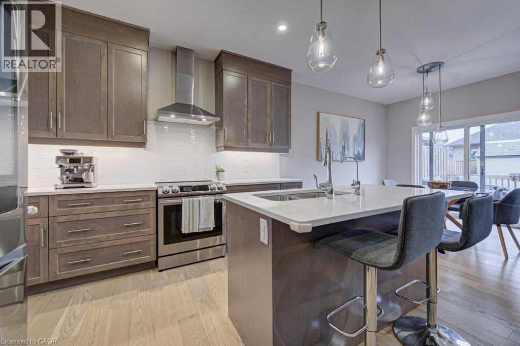 Kitchen featuring wood-finish cabinetry, stainless steel appliances, a white subway tile backsplash, and a central island with a sink and pendant lighting - 15 Matheson Crescent, Innerkip, ON - Indoor Photo Showing Kitchen With Upgraded Kitchen
