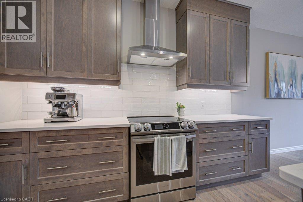 Kitchen featuring wood-finish cabinetry with brushed nickel hardware, stainless steel electric range, stainless steel range hood, white subway tile backsplash, and white countertops - 15 Matheson Crescent, Innerkip, ON - Indoor Photo Showing Kitchen With Upgraded Kitchen