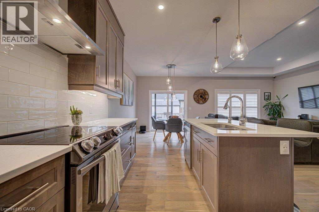 Gourmet kitchen featuring wood-finish cabinetry, light-toned countertops, a subway tile backsplash, stainless steel appliances, and an island with an integrated sink - 15 Matheson Crescent, Innerkip, ON - Indoor Photo Showing Kitchen With Double Sink With Upgraded Kitchen