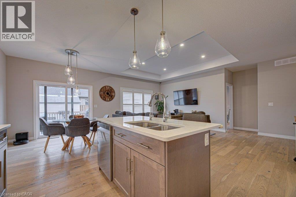 Open-concept living space featuring wood-finish flooring, a kitchen island with integrated sink and stainless steel appliances, modern pendant lighting, a dining area with sliding glass doors, and a l - 15 Matheson Crescent, Innerkip, ON - Indoor Photo Showing Kitchen With Double Sink
