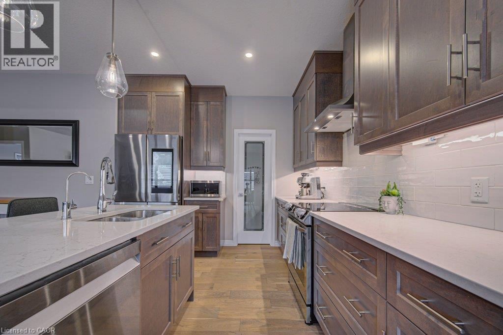 Modern kitchen featuring wood-finish cabinetry, stainless steel appliances, a white subway tile backsplash, light-toned countertops, and wood-finish flooring - 15 Matheson Crescent, Innerkip, ON - Indoor Photo Showing Kitchen With Double Sink With Upgraded Kitchen