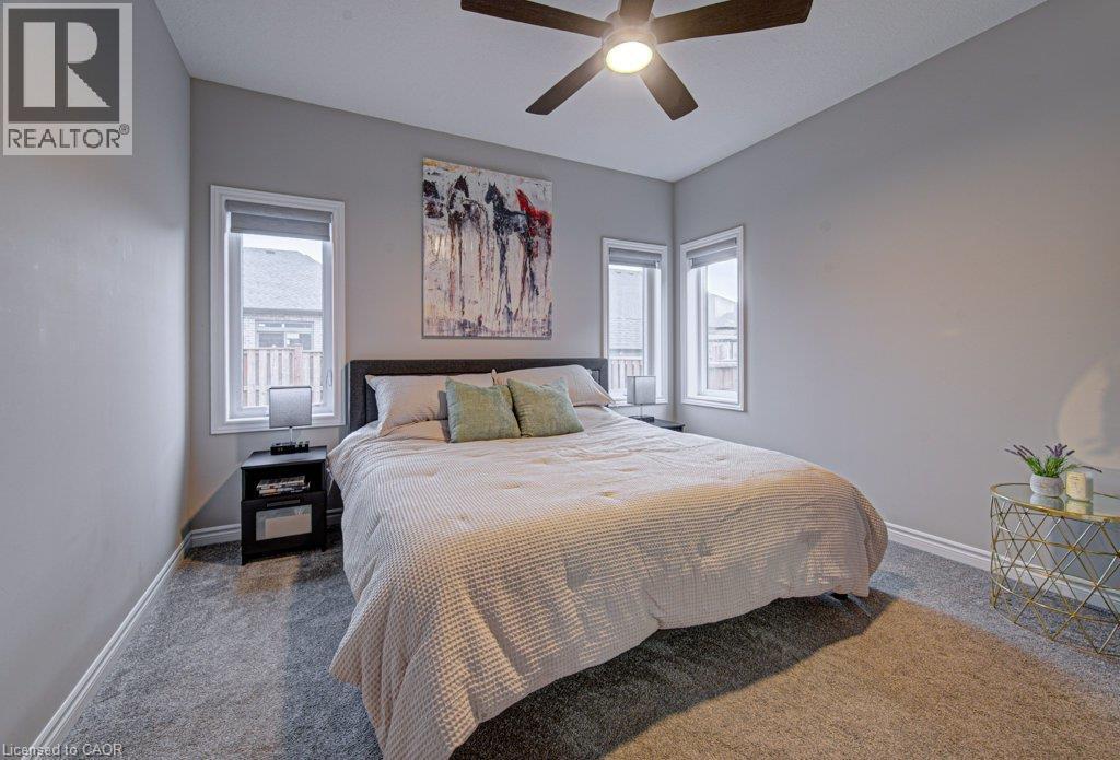 Carpeted room featuring light gray walls, a ceiling fan with integrated lighting, and two windows with white trim - 15 Matheson Crescent, Innerkip, ON - Indoor Photo Showing Bedroom