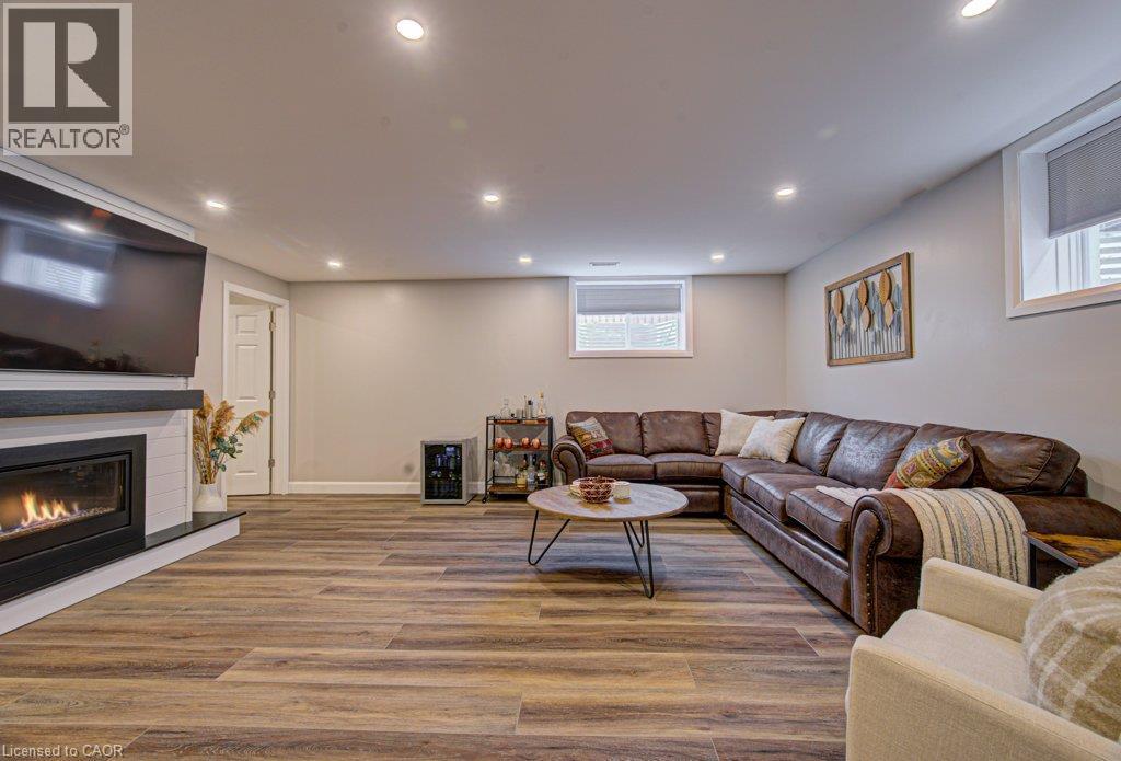 Spacious entertainment room featuring wood-finish flooring, a contemporary fireplace with a white shiplap-style surround, recessed lighting, and multiple windows - 15 Matheson Crescent, Innerkip, ON - Indoor Photo Showing Basement With Fireplace