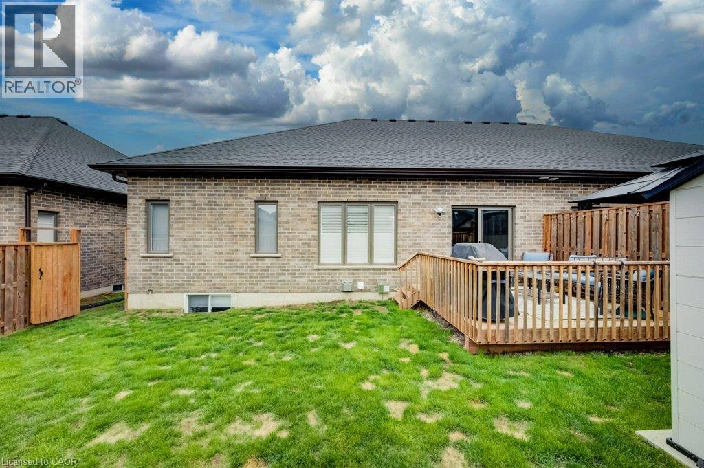Rear exterior featuring a spacious wood deck, light-colored brick facade, multiple windows, a sliding glass door, and a grass lawn - 15 Matheson Crescent, Innerkip, ON - Outdoor With Deck Patio Veranda