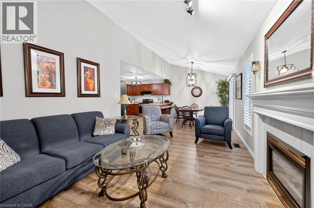 Living area with vaulted ceilings, wood-finish flooring, and a fireplace featuring a white mantel and tile surround - 43 Liam Drive, Ancaster, ON - Indoor Photo Showing Living Room With Fireplace