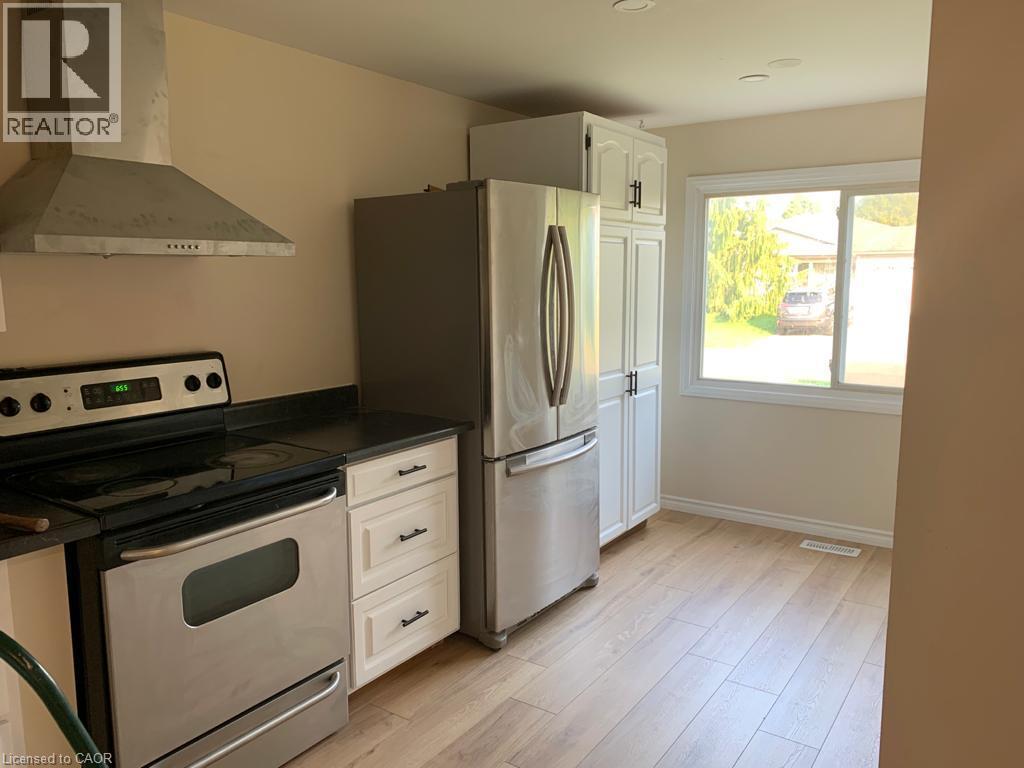Modern kitchen featuring wood-finish flooring, white cabinetry, stainless steel appliances, a range hood, and a large window - 86 Belwood Crescent, Kitchener, ON - Indoor Photo Showing Kitchen