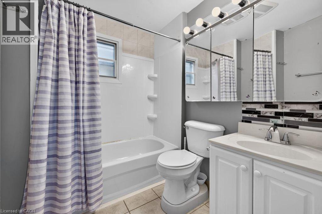 Full bathroom featuring a white vanity with integrated sink, chrome faucet, and mirrored medicine cabinet - 23 Harrison Avenue, Hamilton, ON - Indoor Photo Showing Bathroom