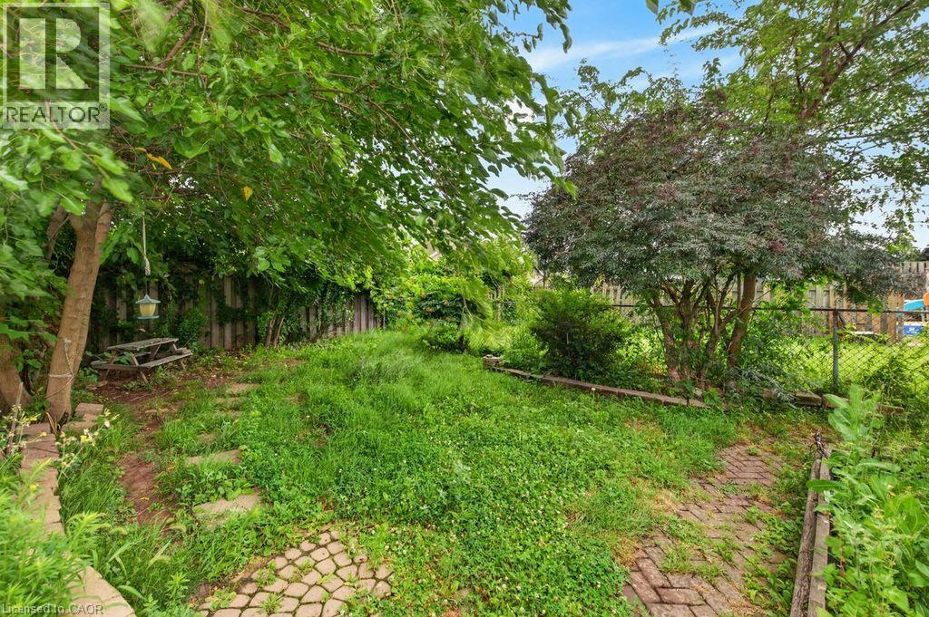 Expansive outdoor space featuring a paved brick pathway, stepping stones, mature trees, and a wooden fence - 23 Harrison Avenue, Hamilton, ON - Outdoor