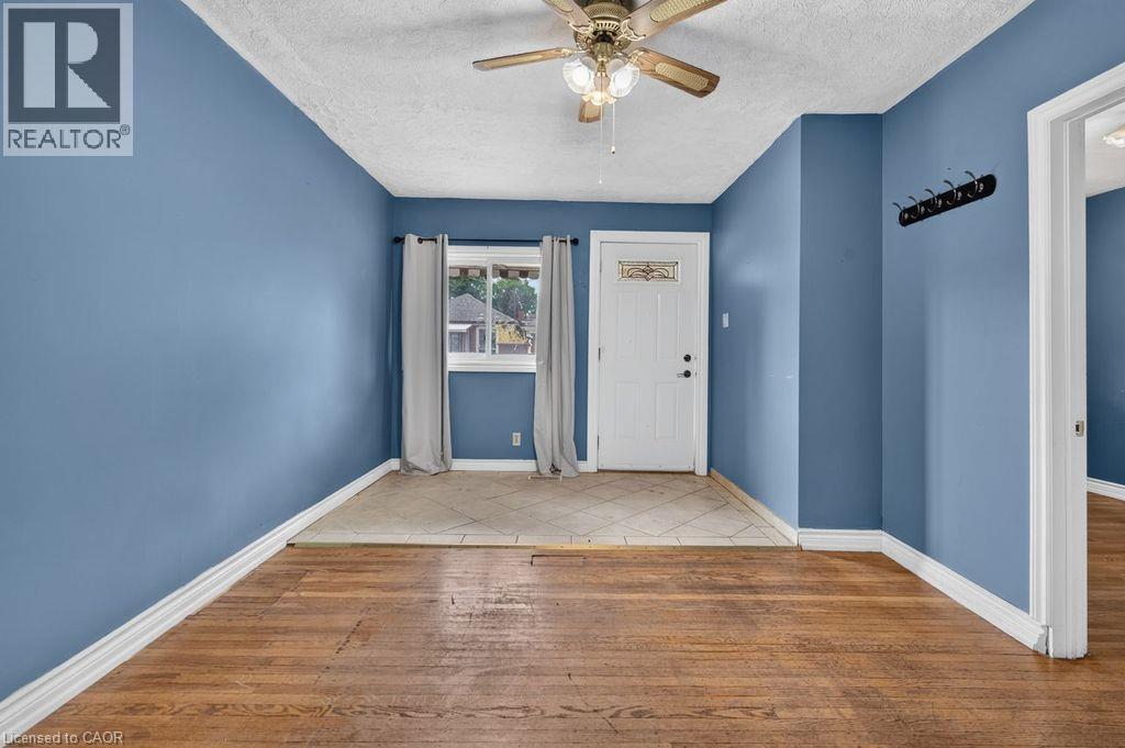 Entry space featuring wood-finish flooring, a tiled entryway, a ceiling fan, and a white paneled door with decorative glass - 23 Harrison Avenue, Hamilton, ON - Indoor Photo Showing Other Room