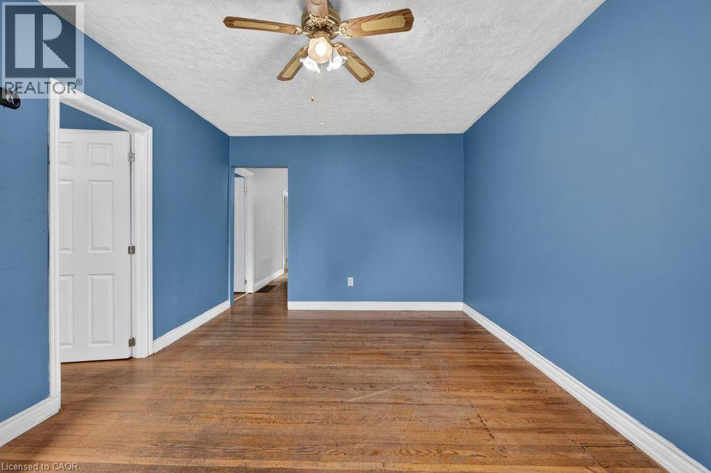 Spacious room featuring wood-finish flooring, a ceiling fan, white baseboards, and a paneled door - 23 Harrison Avenue, Hamilton, ON - Indoor Photo Showing Other Room