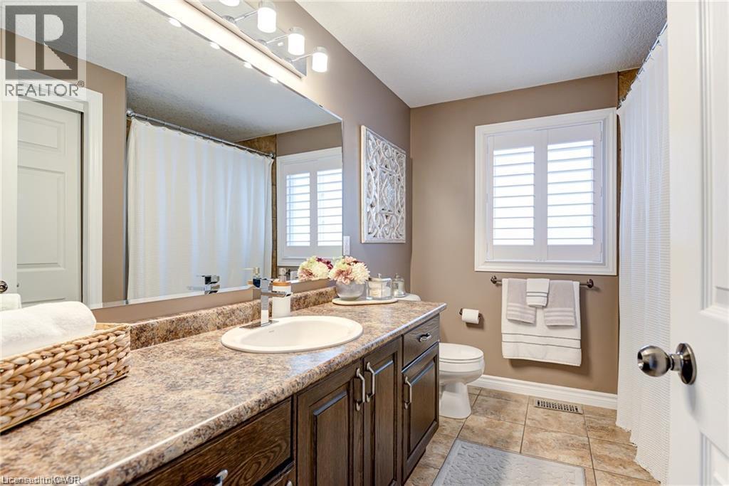 Bathroom featuring a vanity with an integrated sink, a large mirror, a window with plantation shutters, a toilet, and tiled flooring - Upper-313 Featherstone Crescent, Kitchener, ON - Indoor Photo Showing Bathroom