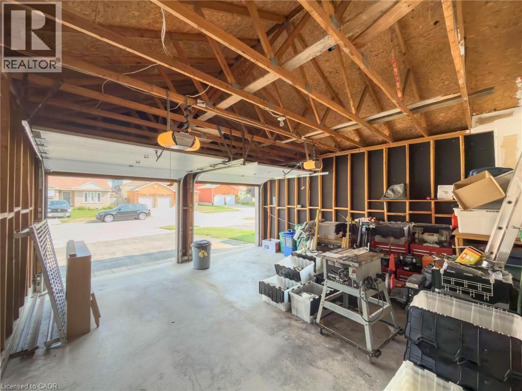Two-car garage with exposed wood beam ceiling, concrete flooring, and automatic overhead door openers - 60 Attwood Drive, Cambridge, ON - Indoor