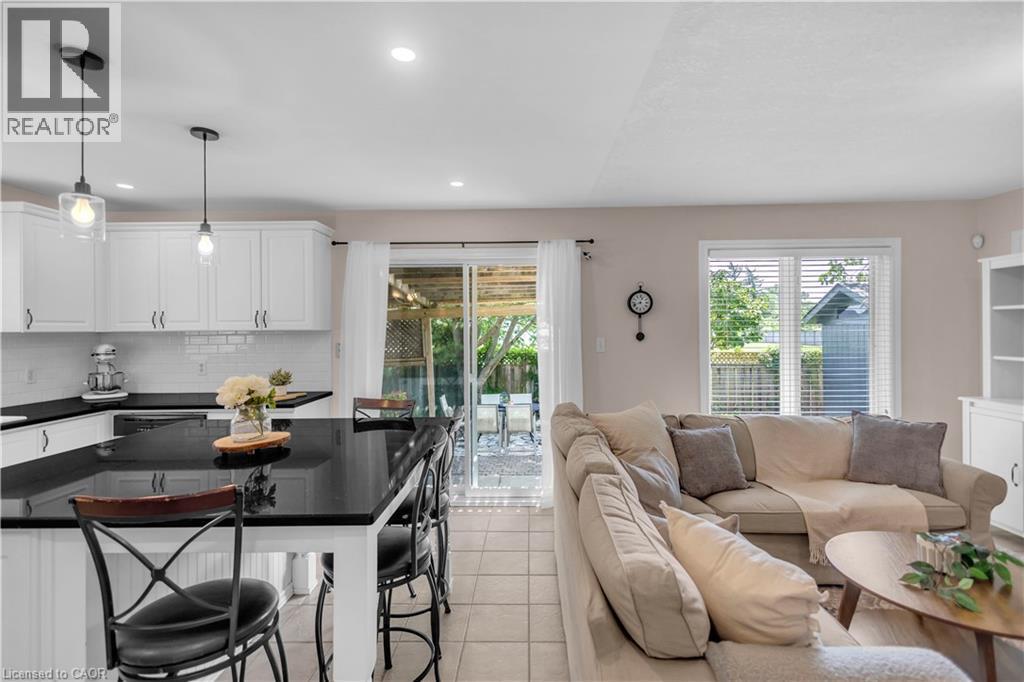Open-concept kitchen and living area featuring a large kitchen island with seating, white cabinetry, black countertops, and a subway tile backsplash - 65 Thistlemoor Drive, Caledonia, ON - Indoor Photo Showing Living Room