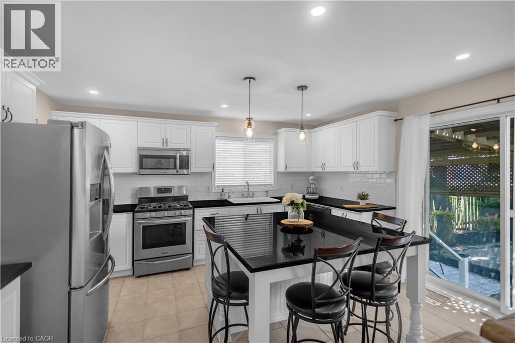 Modern kitchen featuring white cabinetry, stainless steel appliances, a black countertop island, and tile flooring - 65 Thistlemoor Drive, Caledonia, ON - Indoor Photo Showing Kitchen With Upgraded Kitchen