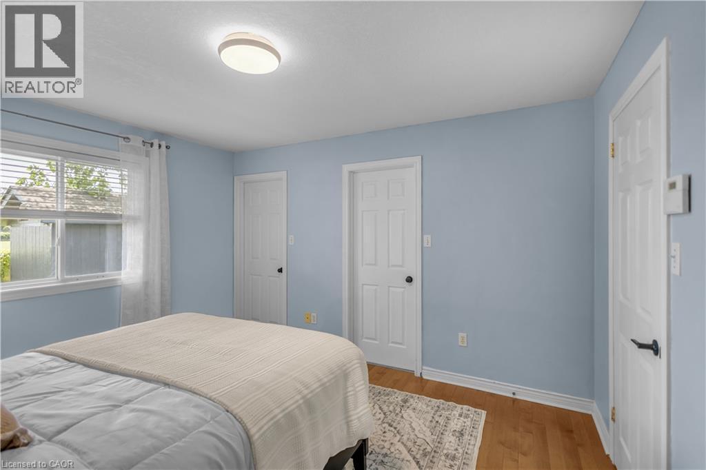 Bedroom featuring a window with blinds, wood-finish flooring, two paneled doors, and a ceiling-mounted light fixture - 65 Thistlemoor Drive, Caledonia, ON - Indoor Photo Showing Bedroom