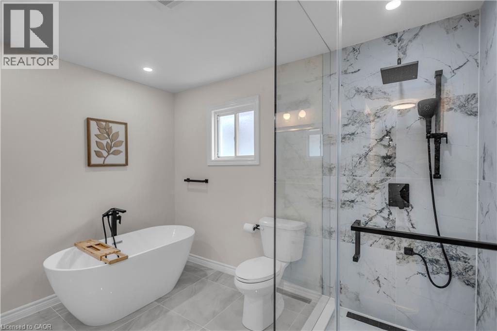 Modern bathroom featuring a freestanding soaking tub with a matte black floor-mounted faucet, a walk-in shower with a glass enclosure and marble-look tile surround, a built-in shower niche, and a rain - 65 Thistlemoor Drive, Caledonia, ON - Indoor Photo Showing Bathroom