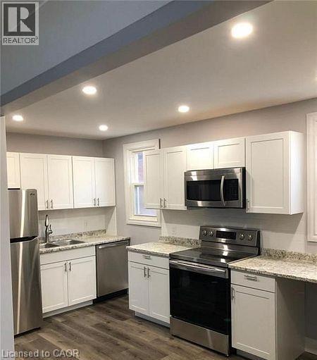Modern kitchen featuring white shaker-style cabinetry, stainless steel appliances, granite-style countertops, wood-finish flooring, and recessed lighting - 84 Ewen Road, Hamilton, ON - Indoor Photo Showing Kitchen With Stainless Steel Kitchen