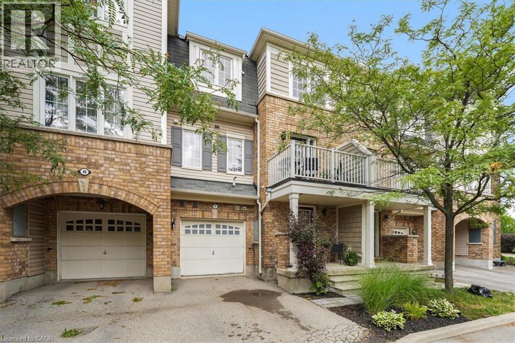 Multi-level exterior featuring brick and siding construction, individual garages with arched entrances, a second-story balcony with white railing, and a ground-floor covered entrance with columns - 7 Sirente Drive Unit# 7, Hamilton, ON - Outdoor With Balcony