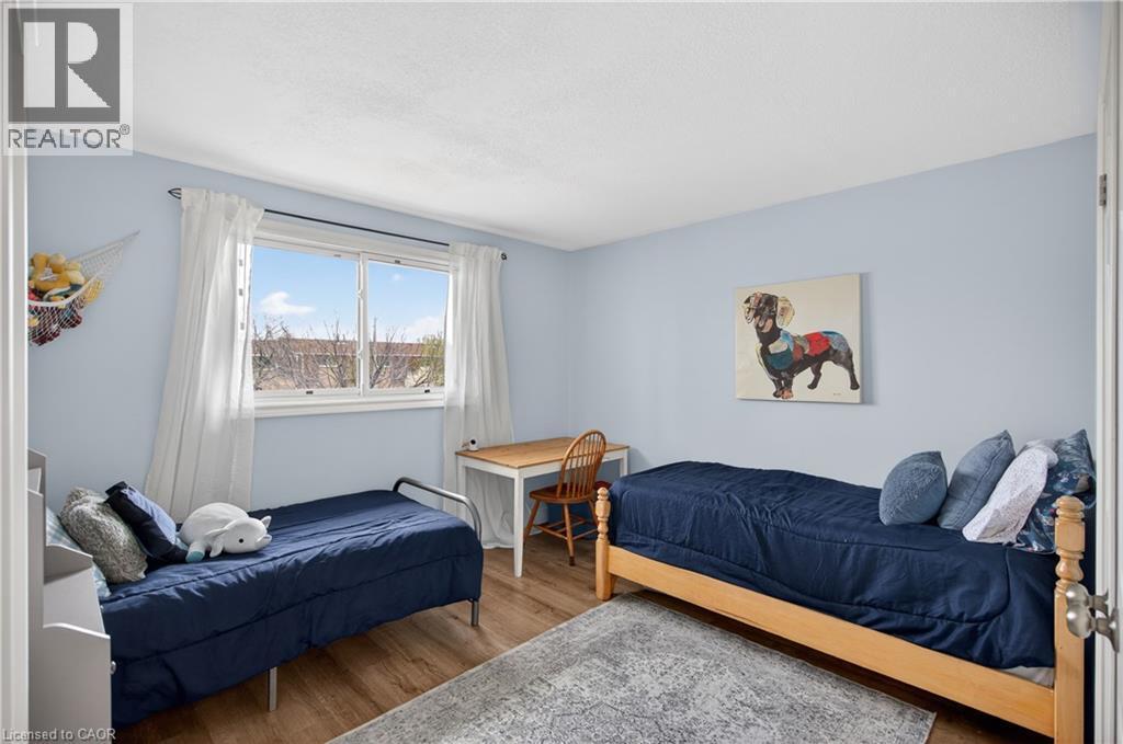 Spacious room featuring wood-finish flooring, a large window, light blue painted walls, and white baseboards - 56 Brookstream Court, Hamilton, ON - Indoor Photo Showing Bedroom