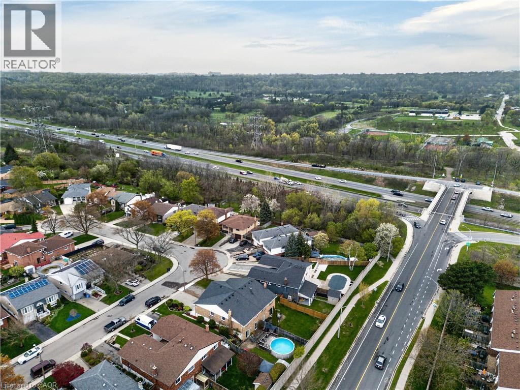 Aerial perspective showcasing a residential neighborhood with varied architectural styles, mature trees, and a highway running parallel - 56 Brookstream Court, Hamilton, ON - Outdoor With View