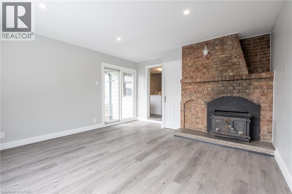 Expansive room featuring a brick fireplace with a wood-burning stove, light wood-finish flooring, and recessed ceiling lighting - 156 Adeline Avenue, Hamilton, ON