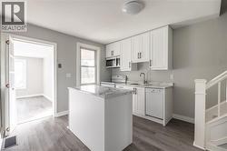 Modern kitchen featuring white cabinetry, a central island with a solid surface countertop, stainless steel appliances, and wood-finish flooring - 