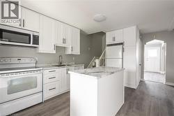 Modern kitchen featuring white cabinetry with dark hardware, a center island with a stone-finish countertop, wood-finish flooring, and white appliances - 