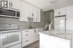 Kitchen featuring white shaker-style cabinetry with matte black hardware, white appliances, and marble-look countertops - 