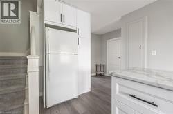 Full-height white cabinetry with black hardware, integrated refrigeration, wood-finish flooring, and a marble-finish countertop - 