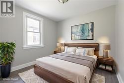 Bright bedroom featuring a double-hung window with white trim, wood-finish flooring, and a ceiling-mounted light fixture - 