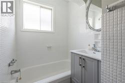 Bathroom featuring white square mosaic tile, a white bathtub, a window with a privacy screen, a gray vanity with chrome hardware, and an ornate wall mirror - 