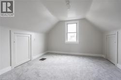 Attic room featuring a single window, two panel doors, sloped ceilings, and light gray carpeting - 