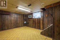 Lower-level room featuring wood-finish wall paneling, patterned flooring, a drop ceiling, and exposed overhead lighting - 