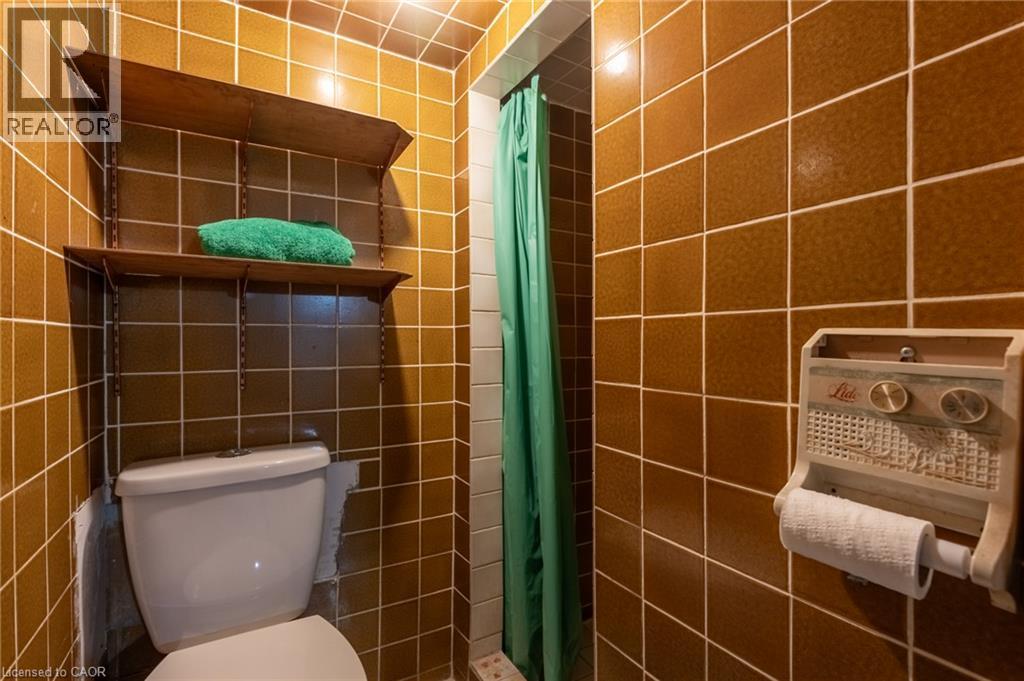 Bathroom featuring brown tiled walls, a white toilet, and a shower area with a green shower curtain - 156 Adeline Avenue, Hamilton, ON - Indoor