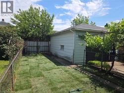 Fenced backyard featuring a newly laid lawn, mature trees, and a detached structure with siding - 