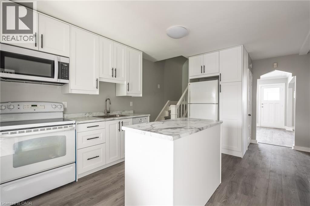 Modern kitchen featuring white cabinetry with dark hardware, a center island with a stone-finish countertop, wood-finish flooring, and white appliances - 156 Adeline Avenue, Hamilton, ON