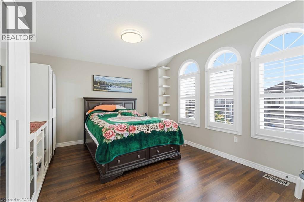 Bedroom featuring three arched windows with plantation shutters, wood-finish flooring, and a built-in shelving unit - 212 Chartwell Circle, Hamilton, ON - Indoor Photo Showing Bedroom