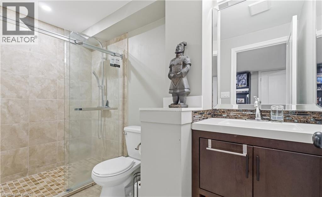 Bathroom featuring a glass-enclosed shower with tile surround and floor, a toilet, and a vanity with a rectangular sink, mosaic tile backsplash, and framed mirror - 212 Chartwell Circle, Hamilton, ON - Indoor Photo Showing Bathroom