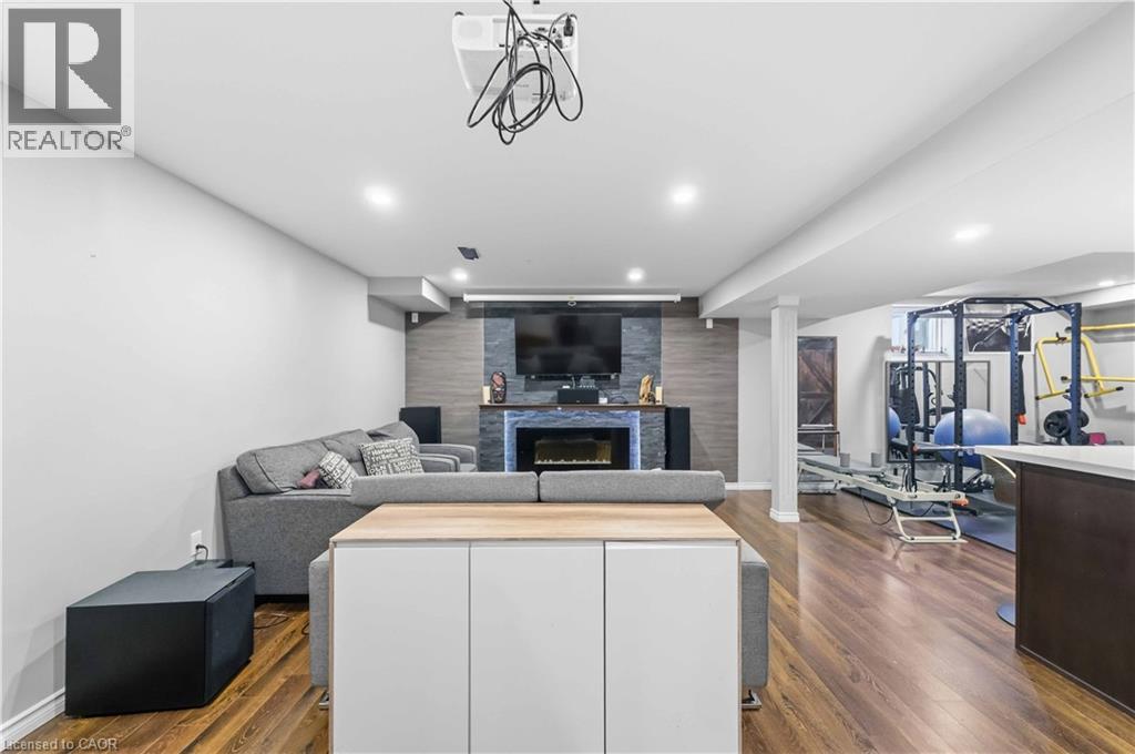 Finished basement featuring wood-finish flooring, recessed lighting, and a modern fireplace with a stone-accented wall - 212 Chartwell Circle, Hamilton, ON - Indoor With Fireplace