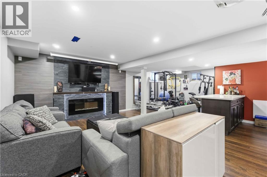 Recreation room featuring a stacked stone fireplace with LED lighting, a built-in media console, wood-finish flooring, and recessed ceiling lights - 212 Chartwell Circle, Hamilton, ON - Indoor Photo Showing Living Room With Fireplace