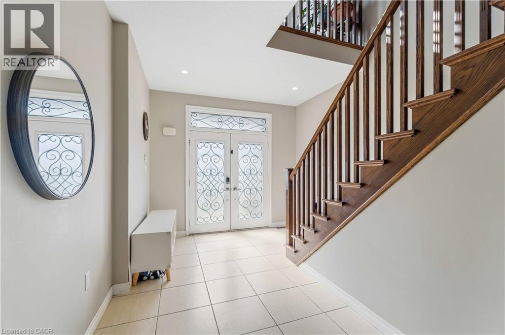Entryway featuring a double door with decorative glass inserts, ceramic tile flooring, and a natural wood staircase with white risers - 212 Chartwell Circle, Hamilton, ON - Indoor Photo Showing Other Room