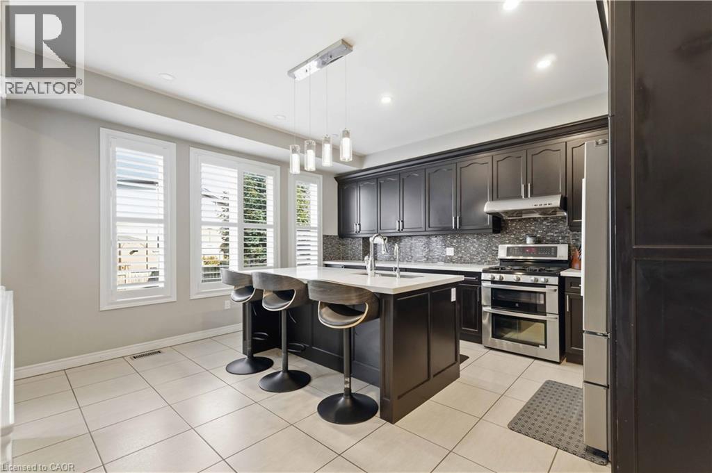 Contemporary kitchen featuring a central island with a light-toned countertop, dark cabinetry, stainless steel appliances, a mosaic tile backsplash, and recessed lighting - 212 Chartwell Circle, Hamilton, ON - Indoor Photo Showing Kitchen With Upgraded Kitchen