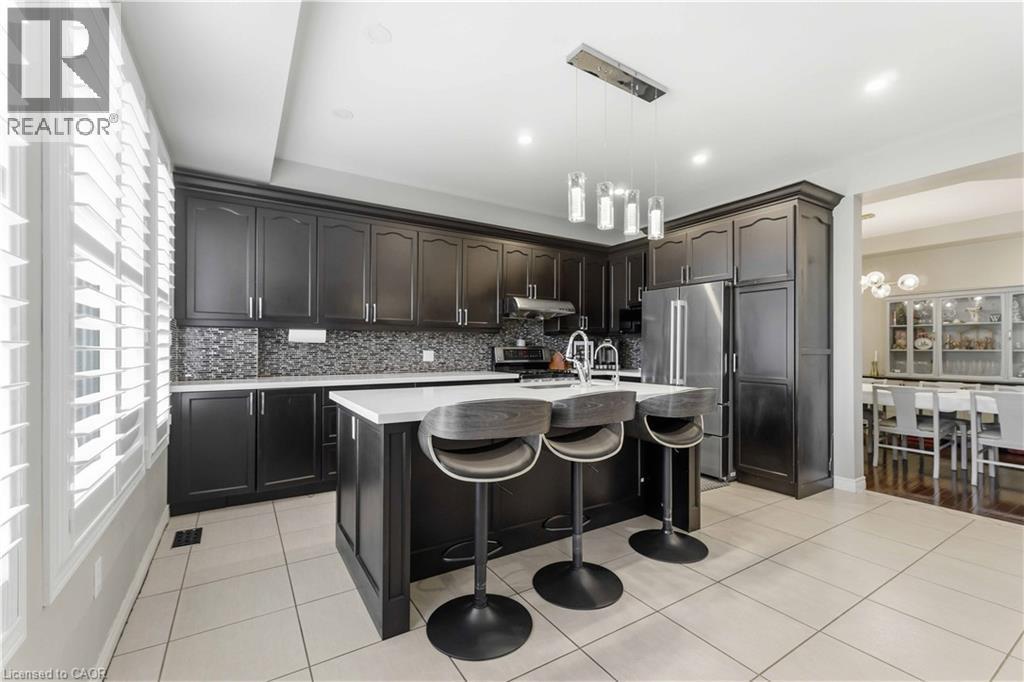 Kitchen featuring dark wood cabinetry, stainless steel appliances, a center island with countertop seating, and a mosaic tile backsplash - 212 Chartwell Circle, Hamilton, ON - Indoor Photo Showing Kitchen With Upgraded Kitchen