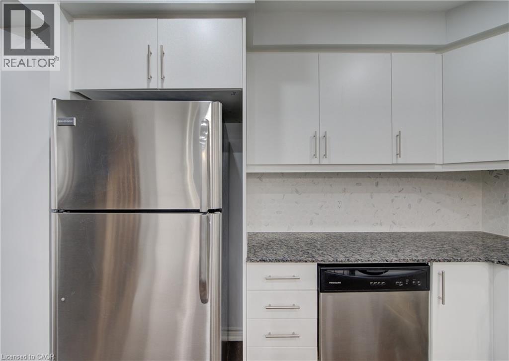 Kitchen featuring stainless steel refrigerator, built-in stainless steel dishwasher, white cabinetry with brushed nickel hardware, light-toned backsplash, and dark granite countertops - 911 Apple Hill Lane, Kitchener, ON - Indoor Photo Showing Kitchen With Stainless Steel Kitchen