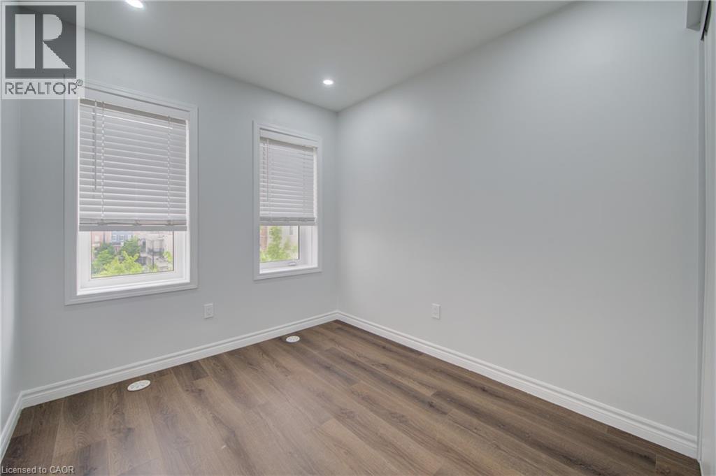 Bright room with wood-finish flooring and two windows featuring white blinds - 911 Apple Hill Lane, Kitchener, ON - Indoor Photo Showing Other Room