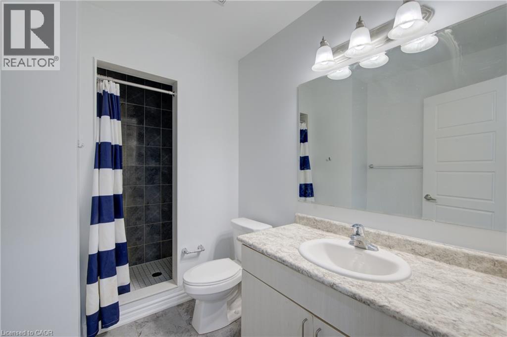 Bathroom featuring a walk-in shower with dark tile surround and a single vanity with an integrated sink and light-colored countertop - 911 Apple Hill Lane, Kitchener, ON - Indoor Photo Showing Bathroom