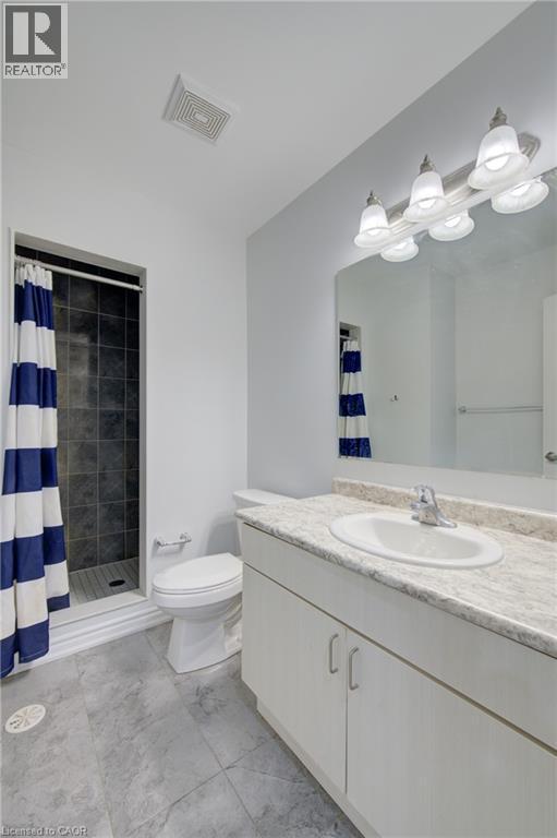 Bathroom featuring a vanity with a white countertop and integrated sink, a large mirror with a five-light fixture, a toilet, and a walk-in shower with dark tile surround - 911 Apple Hill Lane, Kitchener, ON - Indoor Photo Showing Bathroom